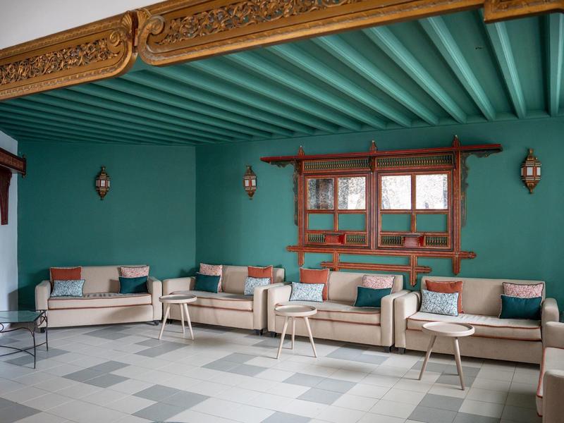 Área de estar elegante con sofás blancos, techo de madera y paredes pintadas de verde en un hotel.