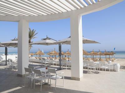 Sonniger Strand mit abgestellten Tischen, Stühlen und Sonnenschirmen unter überdachtem Bereich