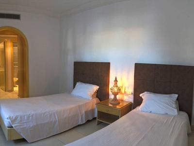 Dwa pojedyncze łóżka z białą pościelą i stolik nocny z lampą w prostej hotelowej sypialni.