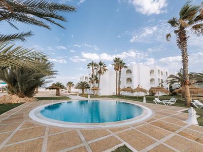 Runder Pool auf gepflasterter Terrasse mit Palmen und weißem Hotelgebäude im Hintergrund
