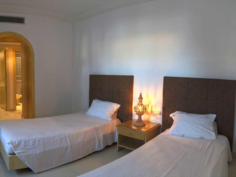 Dwa pojedyncze łóżka z białą pościelą i stolik nocny z lampą w prostej hotelowej sypialni.