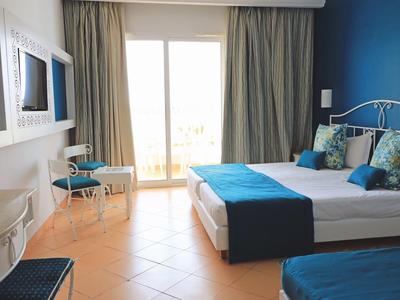 Helles Schlafzimmer mit Doppelbett, blauen Akzenten und Terrassentür mit Vorhängen.