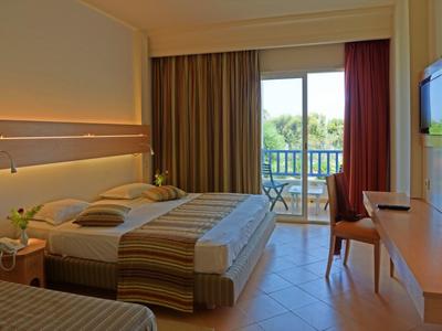 Modernes Hotelzimmer mit zwei Betten, Balkon, Fernseher, Stuhl und Blick auf grüne Landschaft.