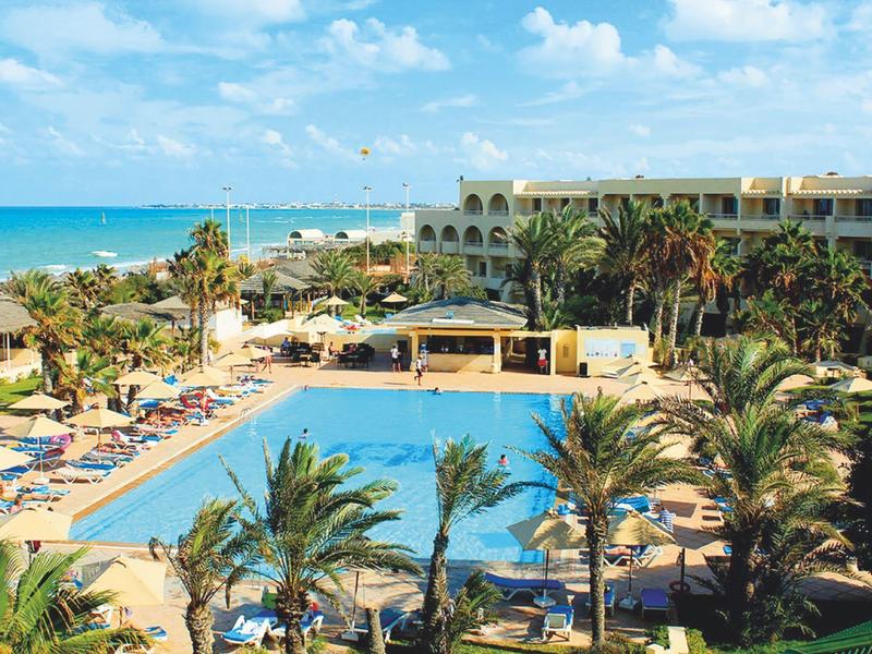 Hotel complex with large pool, palm trees, and direct beach access under clear skies.