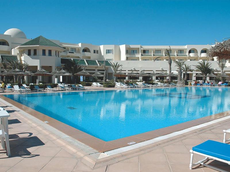 Large outdoor pool with blue water in front of white hotel building and sun loungers