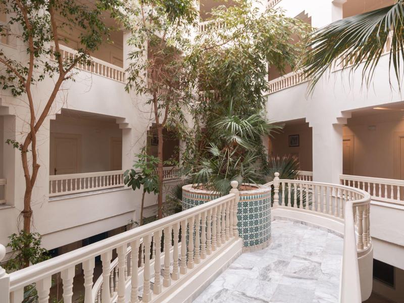 Innenhof mit weißen Geländern, Pflanzen und Arkaden, die ein ruhiges Ambiente schaffen.