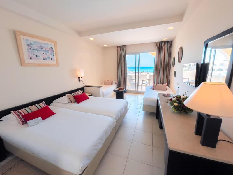 Helles Hotelzimmer mit zwei Betten, Balkon und Meerblick bei Tageslicht.