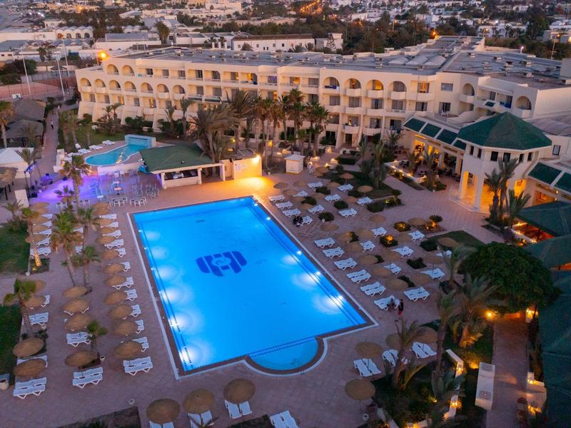 Large hotel pool at sunset with surrounding lounge chairs and hotel building