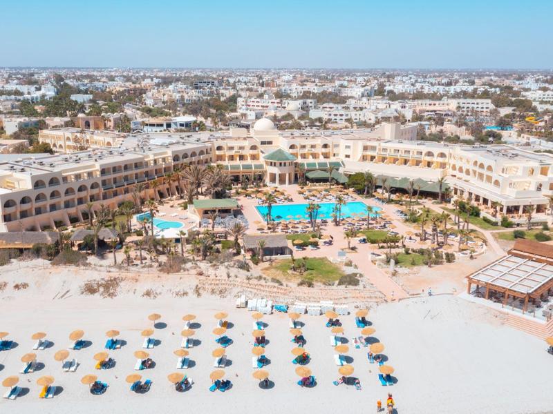 Large hotel resort with pools, sun loungers, and direct access to sandy beach under clear sky.