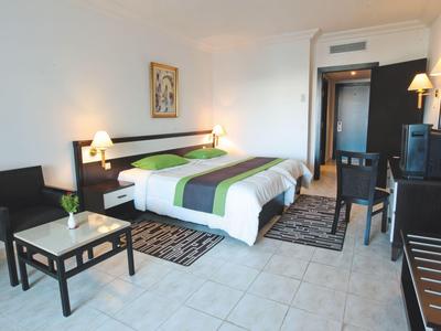 Modern hotel room with double bed, seating area, desk, and simple decor.