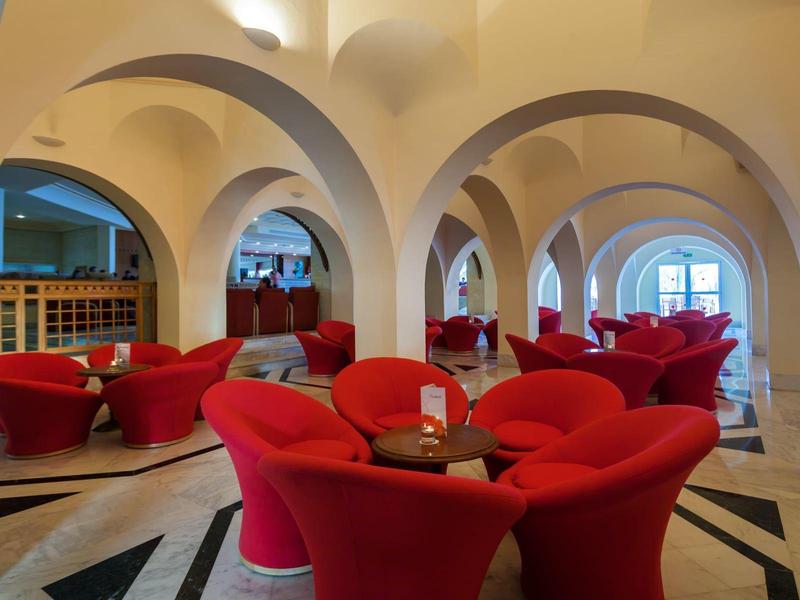 Hotel-Lounge mit roten Sesseln und gewölbten Decken in warmem Licht.