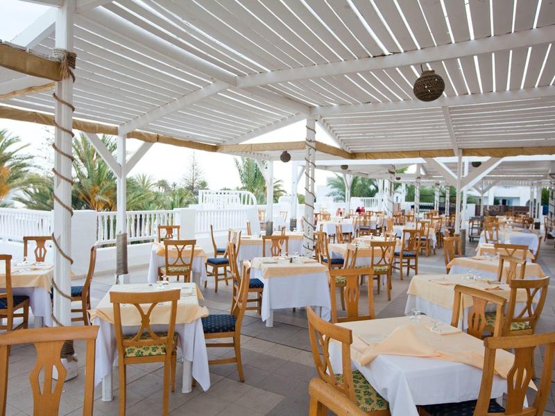 Helles, offenes Restaurant mit Holzmöbeln und weißen Tischen unter einem überdachten Außenbereich.