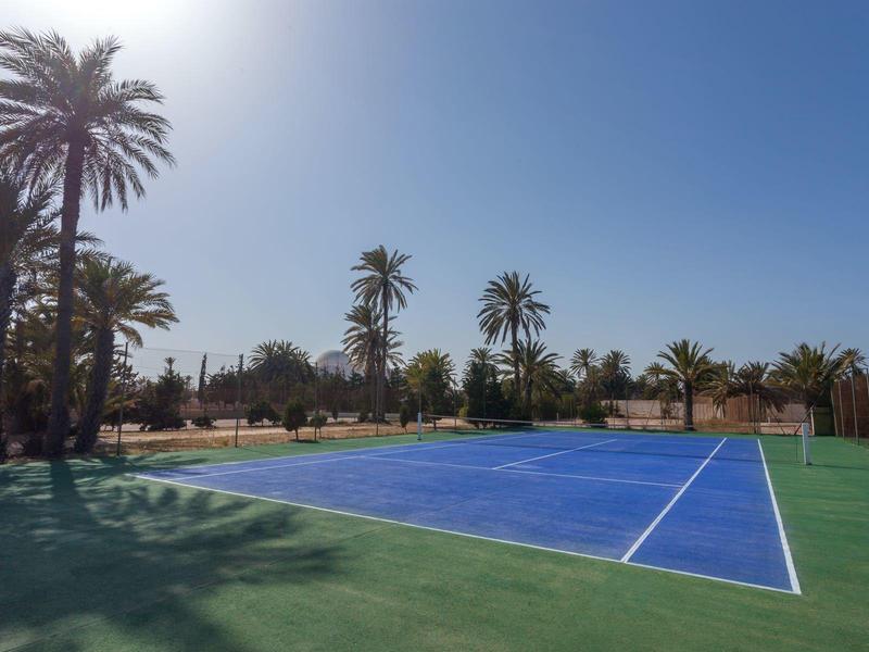 Freiluft-Tennisplatz im Hotel mit blauen und grünen Spielfeldern, Palmen im Hintergrund.