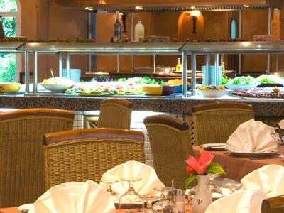 Restaurant mit Buffet und gedeckten Tischen, Stühle aus Korbgeflecht, warmes Licht und Fenster.