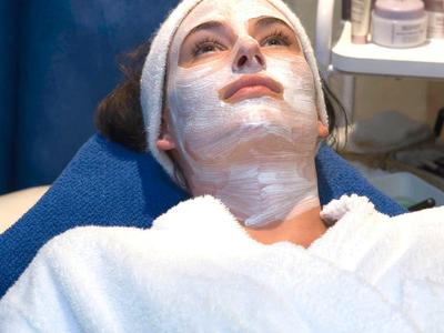 Frau mit Gesichtsmaske und weißem Bademantel liegt entspannt in einer Kosmetikbehandlung.