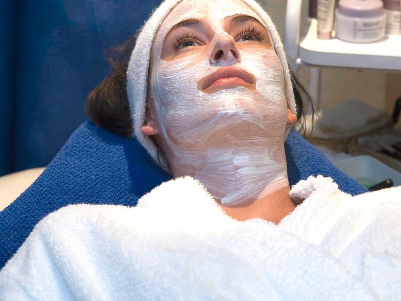 Frau mit Gesichtsmaske und weißem Bademantel liegt entspannt in einer Kosmetikbehandlung.