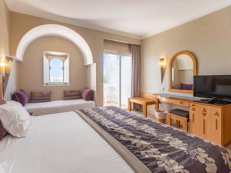 Schlafzimmer mit Doppelbett, Sitzbank unter Bogenfenster, Holzmöbeln und Balkon.