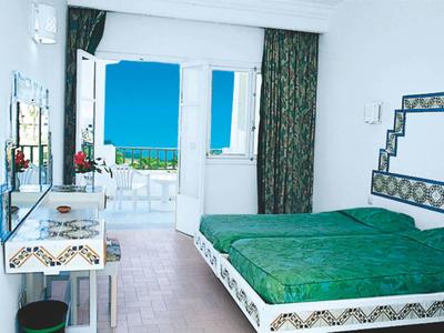 Lichte hotelkamer met groen bed, balkon en uitzicht op zee.