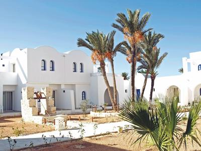 Witte gebouwen met blauwe deuren en palmbomen onder een heldere lucht in een hotelgebied.