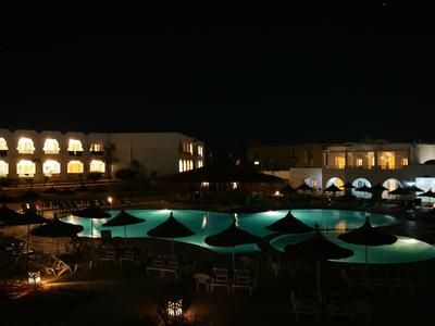 Hotelzwembad verlicht in de nacht met parasols en omringende gebouwen.