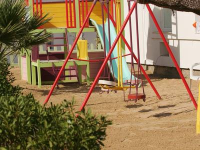 Kleurrijke speeltuin met houten huis en schommel buiten naast een hotel.