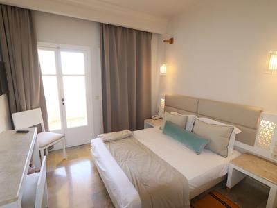 Helles Schlafzimmer mit großem Bett, Nachttischen und Fernseher an der Wand.