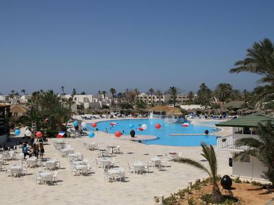 Großer Außenpool mit Liegestühlen und Palmen in einem Hotelresort bei klarem Himmel.