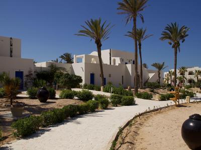 Witgekalkte gebouwen omgeven door palmbomen en een gebogen pad onder een heldere hemel.