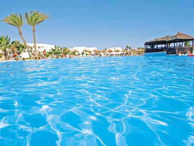 Groot zwembad met helder blauw water, palmbomen en ligstoelen onder een blauwe lucht.