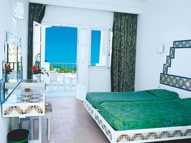 Lichte hotelkamer met groen bed, balkon en uitzicht op zee.