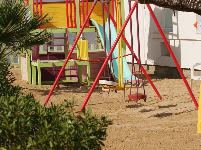 Kleurrijke speeltuin met houten huis en schommel buiten naast een hotel.