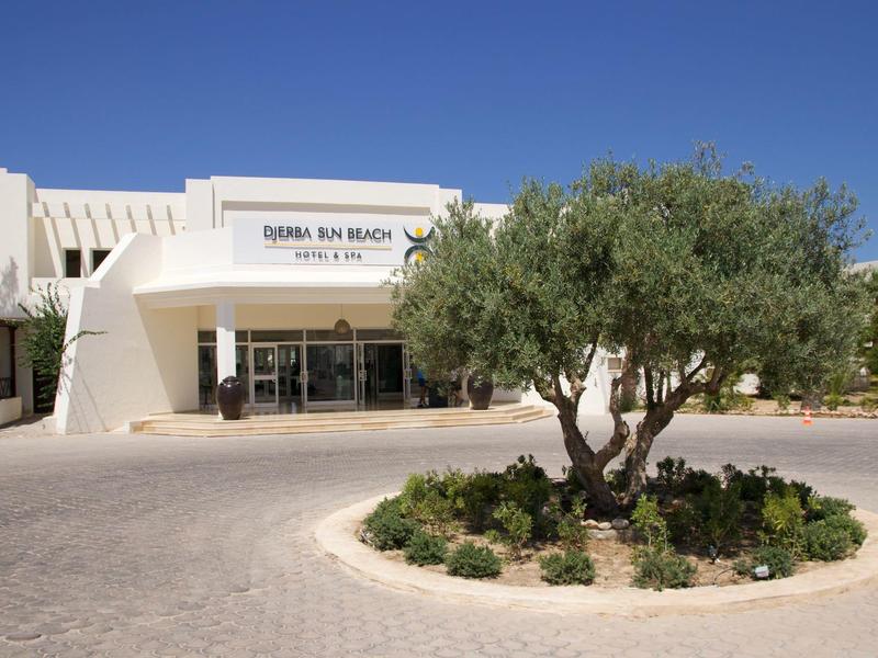 Hotelgebouw met witte gevel, aangelegde binnenplaats en heldere blauwe lucht.