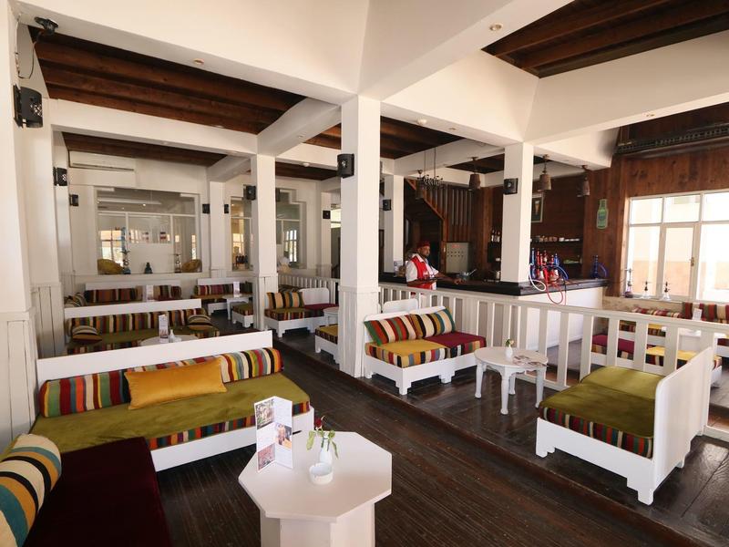 Licht rustiek restaurant met houten meubels en kleurrijke kussens.