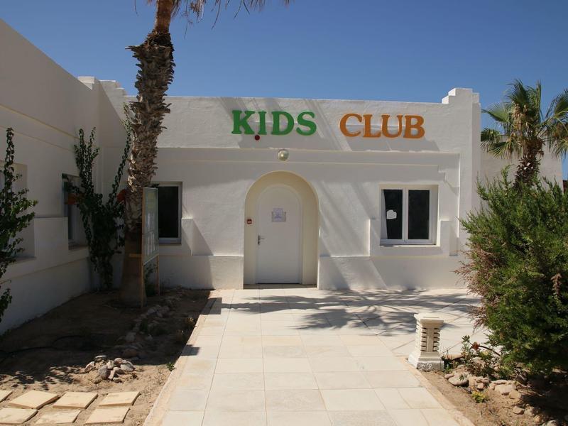 Ingang van kinderclub met witte muren en palmbomen langs het pad.