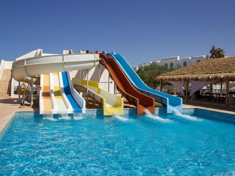 Vier kleurrijke glijbanen leiden naar een groot zwembad naast een overdekte zithoek.