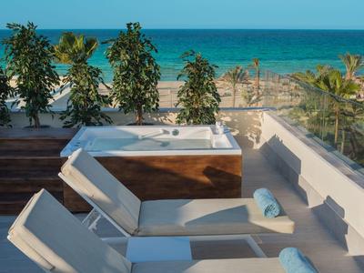 Moderner Hotelpool mit Liegestühlen und Meerblick, umgeben von grünen Pflanzen und Palmen.