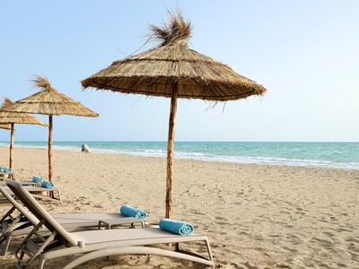 Empty lounge chairs with thatched umbrellas on sandy beach by calm sea.