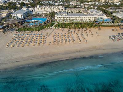 Strand mit Reihen von Sonnenschirmen vor einem großen Hotel und türkisem Meer.