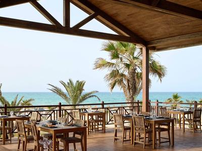 Terraza cubierta con mesas y sillas de madera con vista a palmeras y el mar.