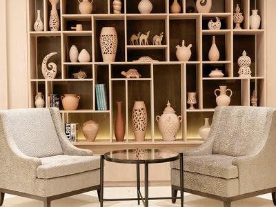 Two beige armchairs with a round glass table between them, a shelf with decorative vases in the background.