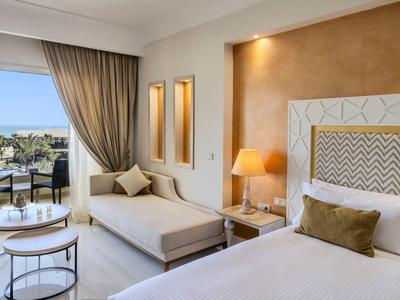 Modernes Hotelzimmer mit gemütlichem Bett, gemütlicher Sitzecke und Balkon mit Meerblick.