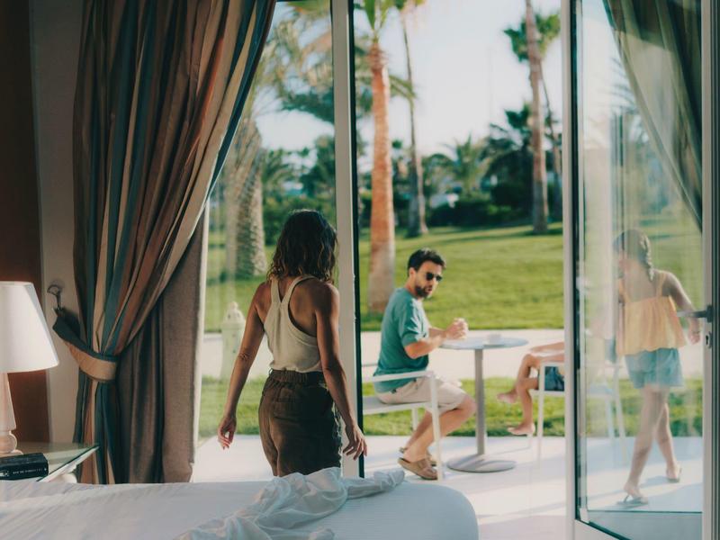 Pareja disfrutando de un desayuno en el balcón con vistas al jardín en un hotel soleado.