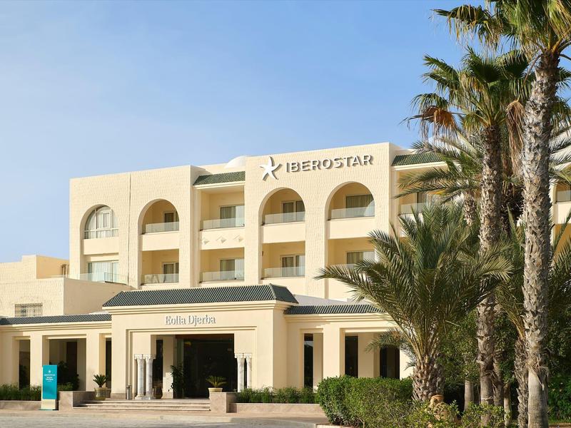 Edificio de hotel con arcos y palmeras bajo cielo despejado.