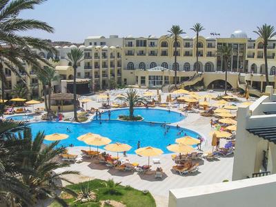 Hotel mit großem Pool, Palmen und vielen gelben Sonnenschirmen am Poolbereich.