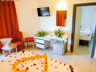 Helles Hotelzimmer mit roten Vorhängen, Schreibtisch, Stühlen und Blick ins Schlafzimmer.