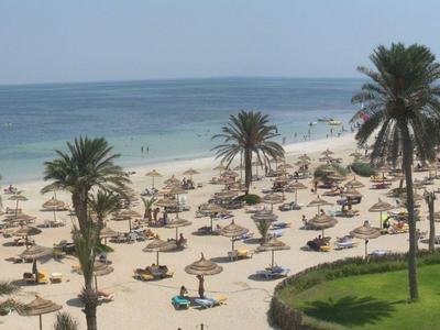 Sandstrand mit Sonnenschirmen, Palmen und klarem Meer bei Sonnenschein.