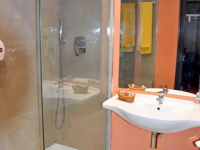 Modernes Badezimmer mit ebenerdiger Dusche, weißem Waschbecken und orangen Wandakzenten.