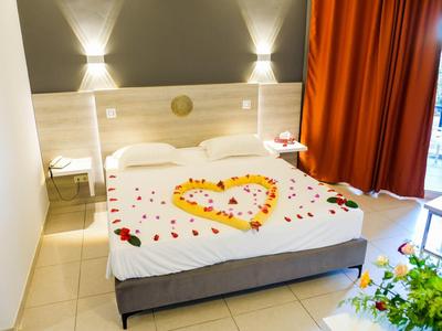 Hotelzimmer mit Doppelbett, Herz aus Blütenblättern und orangenen Vorhängen neben Balkon