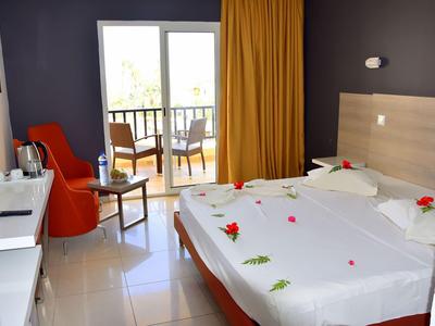 Modernes Hotelzimmer mit Doppelbett, orange Stuhl, Balkon und gelben Vorhängen.