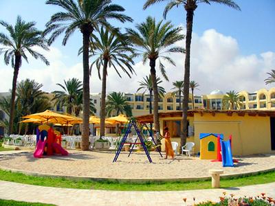 Ein Hotelspielplatz mit Sand, Schaukeln, Rutschen und Palmen bei sonnigem Wetter.
